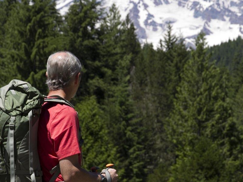 A man with a backpack standing on a trail looking towards Mount 雷尼尔山